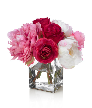 A mixed bouquet of peonies and roses in a glass rectangular vase. Shot against a bright white background. There is a path which may be used to delete the reflection if desired. Extremely high quality faux flowers.