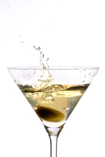 Green olive splashing in a glass of Martini.