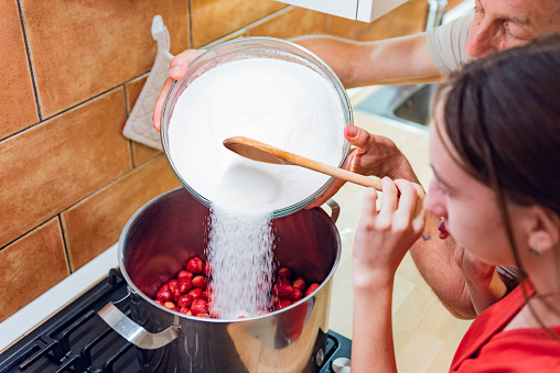 Teenage Girl in Domestic Kitchen with a Help of Father Pouring Sugar on Strawberries to Make a Delicious Sweet Jam