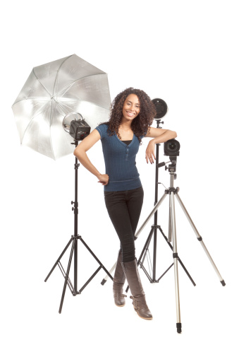 Subject: A young black woman photographer standing with her camera and lighting equipment, proud of her entrepreneurial photography small business venture. Isolated on a white background.