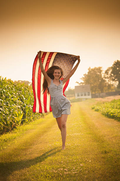 patriotique teen fille courir à travers champ de ferme agitant le drapeau des états-unis - child flag fourth of july little girls photos et images de collection