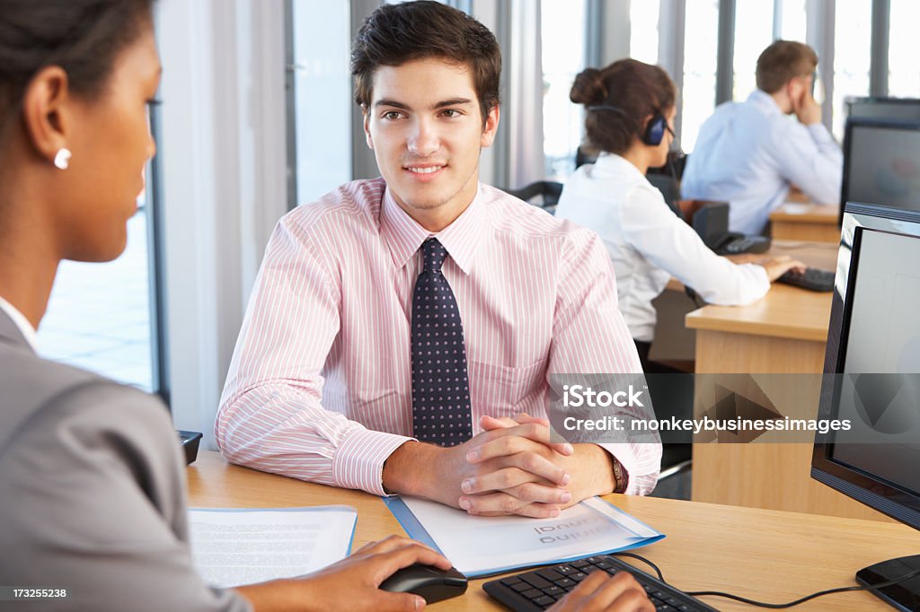 Two coworkers siting in a desk at work Smiling New Employee Starting Work In Busy Office. Adult Stock Photo