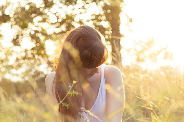 Pensive young woman at summer sunset in the field