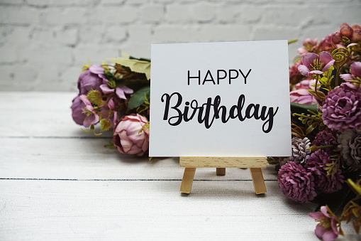 Happy birthday text on wooden easel standing on white brick wall and wooden background