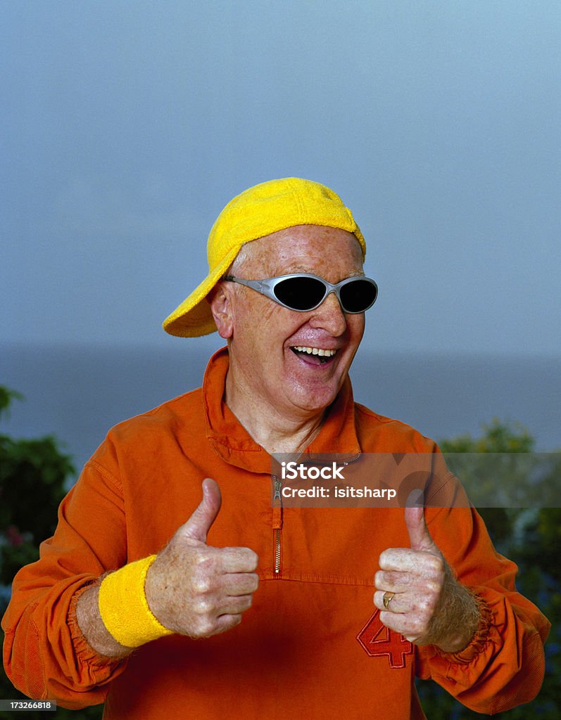 Mature Man Mature man, aged 60-65 years wearing a yellow cap, sunglasses and an orange tracksuit top, laughing. 60-64 Years Stock Photo