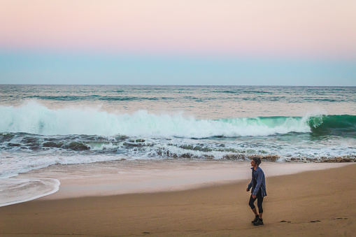 Sayulita, Nayarit Mexico, October 30 2023 woman walking on the beach at sunrise with pink sky in sayulita nayarit