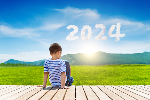 Little boy sitting on wooden sidewalk with 2024 year written on blue sky