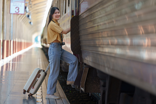 Young businesswoman standing on train door peeking out looking for somebody in a railway station - Portrait of beautiful traveler woman getting on the train - Travelling concept.