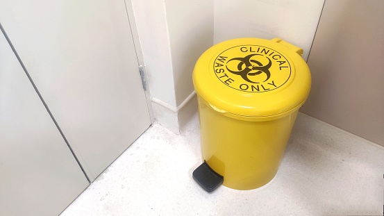 A yellow bin labeled clinical waste only in a hospital room