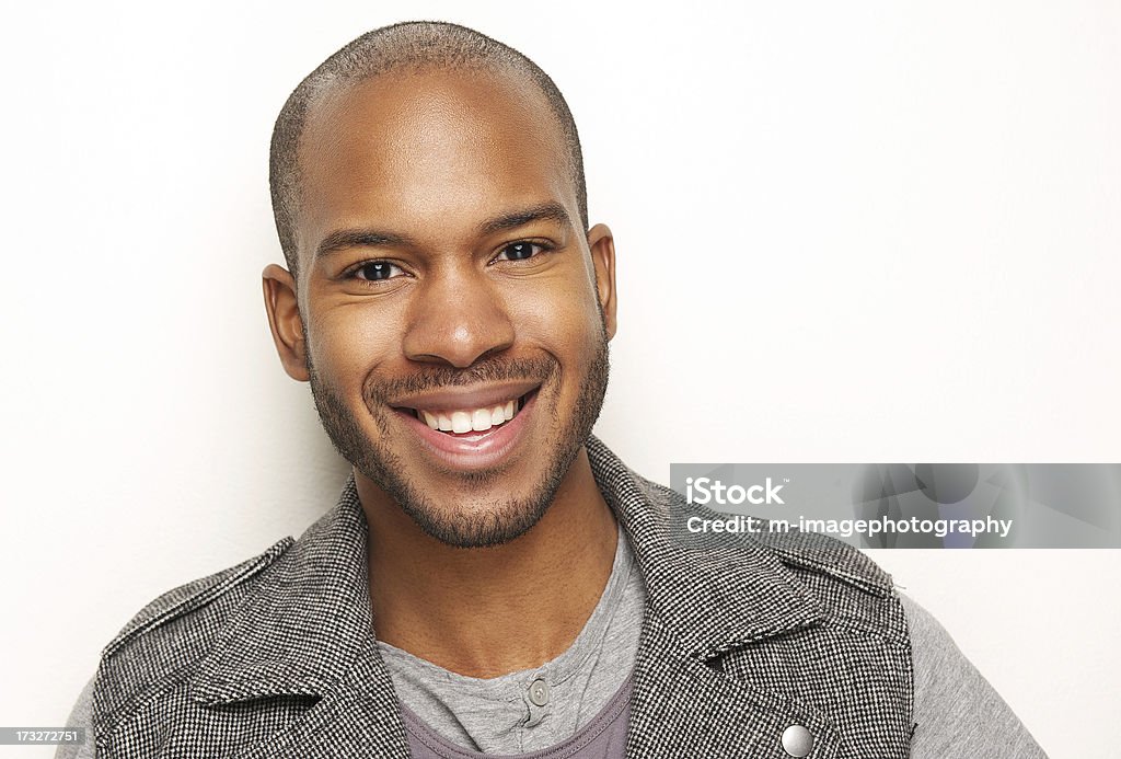 Close-up of smiling young, dark-skinned man Close-up portrait of a handsome young black man smiling against white background Men Stock Photo