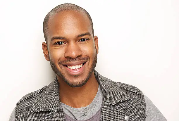 Close-up portrait of a handsome young black man smiling against white background