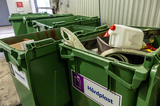 Stockholm, Sweden Large green recycling bins for hard plastics in a car repair shop and a sign in Swedish saying Hard Plastics.