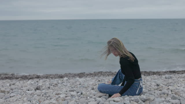 Teenage girl sitting on Lyme Regis Fossil Beach in Dorset, United Kingdom