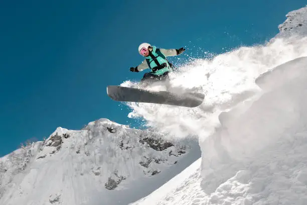Fast girl snowboarder jumps from springboard high in mountains. Winter sports concept