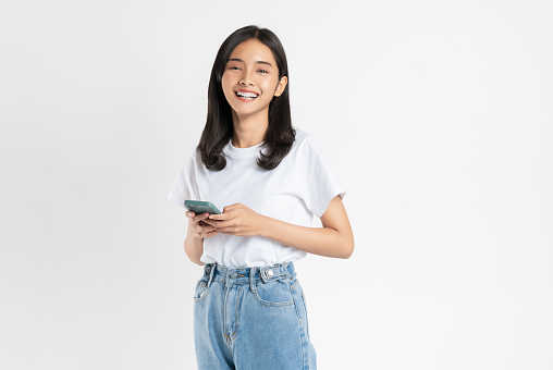 Beautiful Asian woman holding smartphone and smiling on white background.
