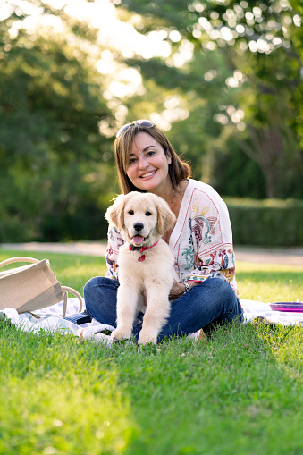 Latin woman with her dog in a public park sitting on the grass looking at camera