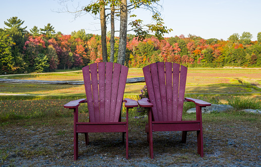Two red wooden muskoka chairs in a park in autumn, fall season, Garden furniture. Sunny and warm fall season