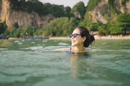 POV asian woman having fun in beautiful sea with sunglasses ,Portrait of happy cheerful woman in bikini floating in tropical paradise Beach
