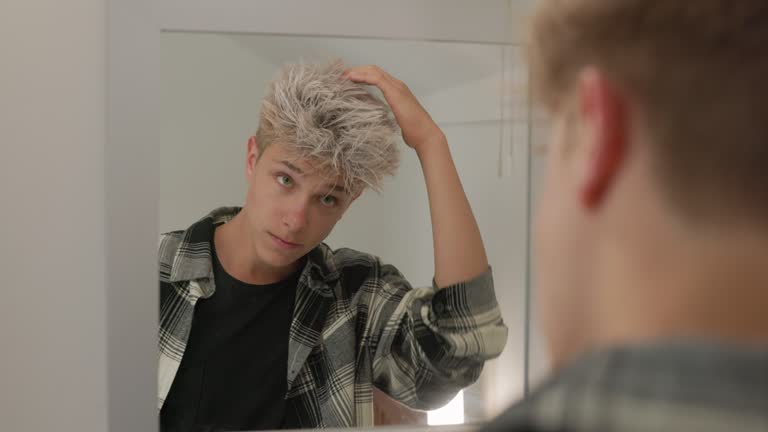 Teenage boy styling his dyed hair in front of the mirror