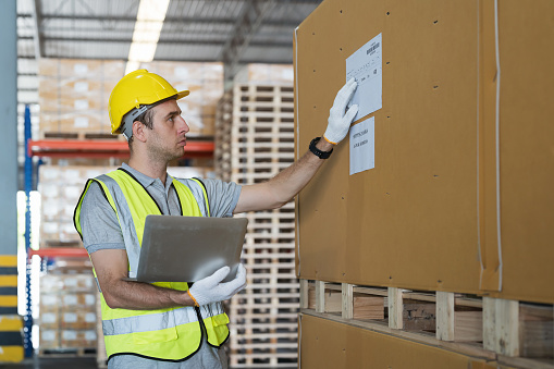 Male warehouse worker inspecting quality of boxes on shelf pallet in the storage warehouse. Man worker working in the warehouse