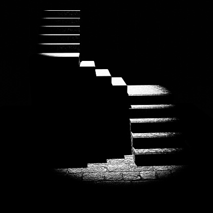 An outside staircase runs diagonally along the house wall and casts shadows on the wall and the paved floor - in black and white.