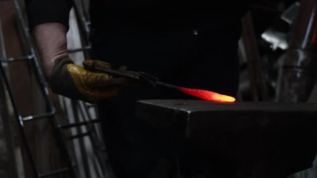 The blacksmith hits the hot workpiece on the anvil with a hammer
