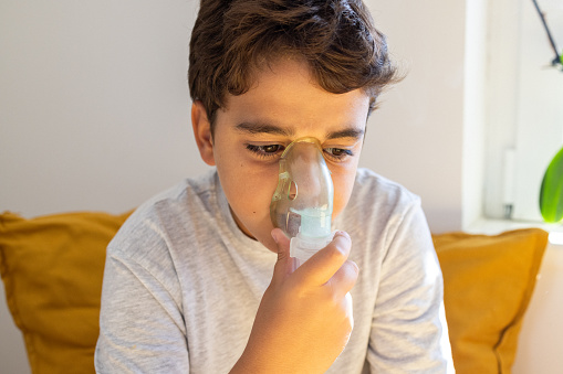 11 year's old asthmatic Caucasian boy, sitting on a bed, while holding an oxygen mask, to help him breath better