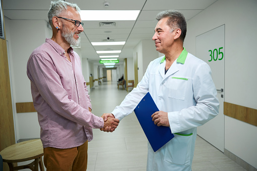 Doctor greets a man in a bright hospital corridor, they shake hands