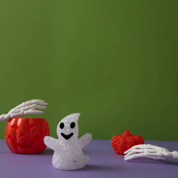 istock Pumpkins for Halloween with a ghost on a purple background with hand bones with copy space on a green background. Minimal aesthetic concept. 1732997940
