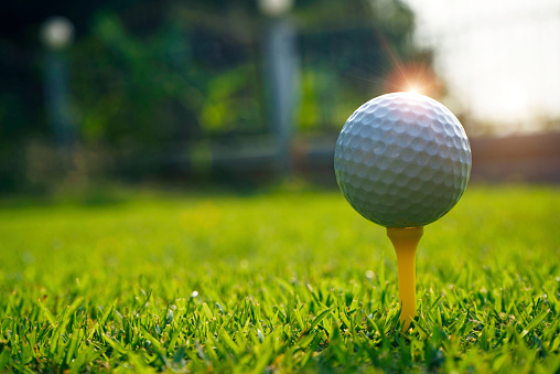 Golf ball on tee in the evening golf course with sunshine background.