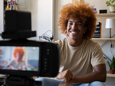 Young African American man recording video for social networks with a camera in an apartment. High quality photo