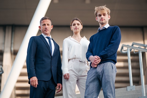 Three corporate professionals standing side-by-side on stairs in formal attire