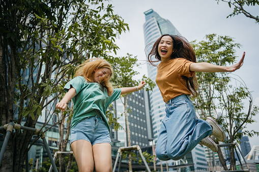 Two smiling friends are joyfully jumping in the city park.