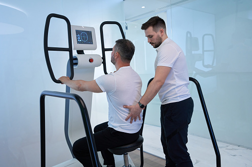 Adult male training in seated position on multi-axis motorized platform under guidance of physiatrist