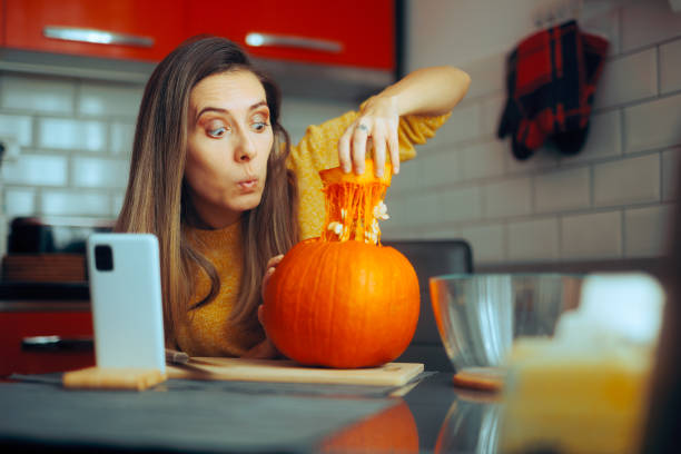 istock Woman Scooping the Seeds from a Pumpkin Following an Online Tutorial 1733056642