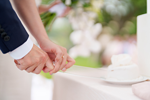 A newlywed couple cuts their cake together during a garden ceremony. Soft focus image.
