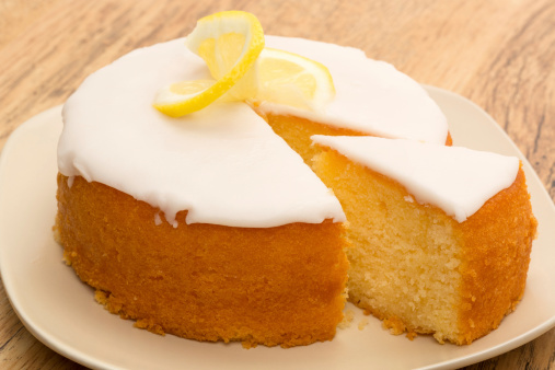 A whole lemon drizzle cake with a slice taken out.
