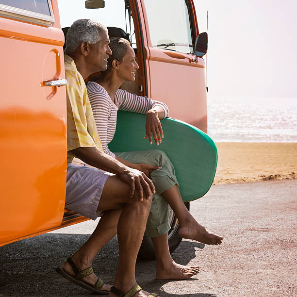 Beach Couple A smiling senior couple sitting on the side of an orange van on the beach in Santa Monica, California... lypsela2013 stock pictures, royalty-free photos & images