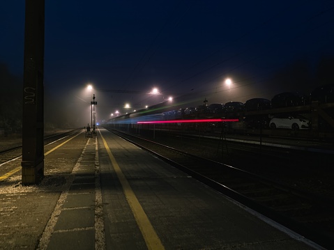 Empty railway station platform at night, long exposure with light trails, car transport train in the background