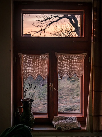 Vintage rural wooden window with curtains from the inside during sunset
