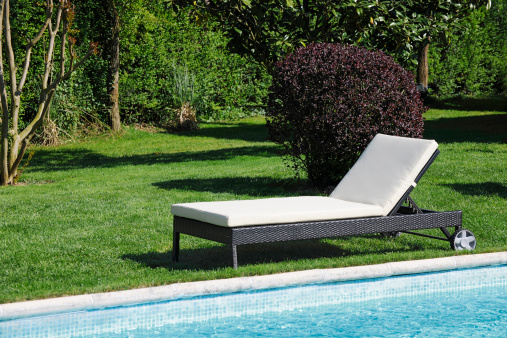 Wooden reclining chair near the swimming pool in garden. 