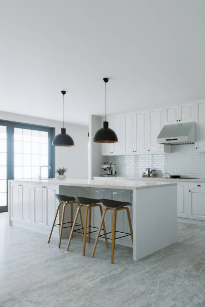 istock Stylish white kitchen with island, black chandelier, appliances and utensils. Kitchen with common area, kitchen appliances and white marble. 3D rendering 1733148014