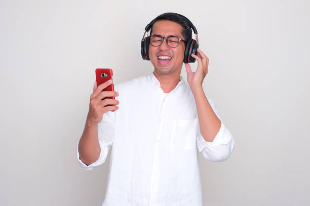 erwachsener asiatischer mann zeigt glücklichen ausdruck beim hören von musik mit kopfhörern - menari stock-fotos und bilder