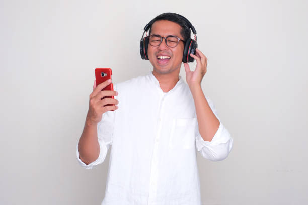 hombre asiático adulto que muestra una expresión feliz al escuchar música con auriculares - menari fotografías e imágenes de stock