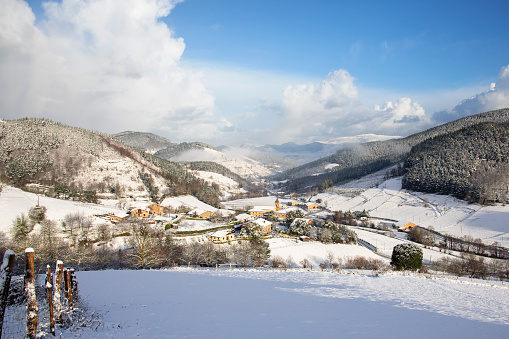 Panoramic view of beautiful white winter wonderland scenery in the Alps with snowy mountain summits reflecting in crystal clear mountain lake on a cold sunny day with blue sky and clouds.