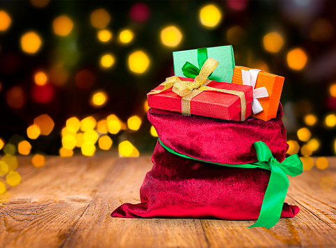 Christmas gifts in a red bag on a wooden table with bokeh background and copy space