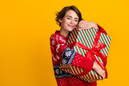Photo of satisfied girl with bob hairstyle dressed sweatshirt embrace present box on christmas eve isolated on yellow color background.