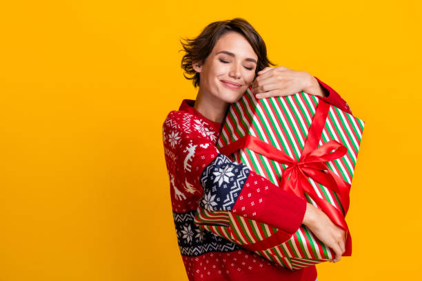 zdjęcie zadowolonej dziewczyny z fryzurą bob ubrana bluza obejmuje pudełko na prezent w wigilię na białym tle na żółtym tle - beautiful women gift christmas zdjęcia i obrazy z banku zdjęć