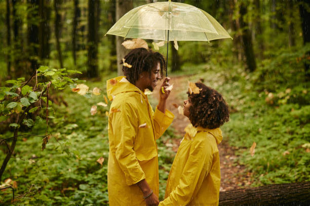 coppia nera felice che parla sotto l'ombrello in una giornata piovosa. - candid women african descent umbrella foto e immagini stock