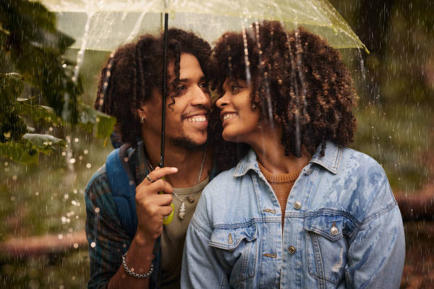 coppia nera felice sotto l'ombrellone in un giorno di pioggia. - candid women african descent umbrella foto e immagini stock